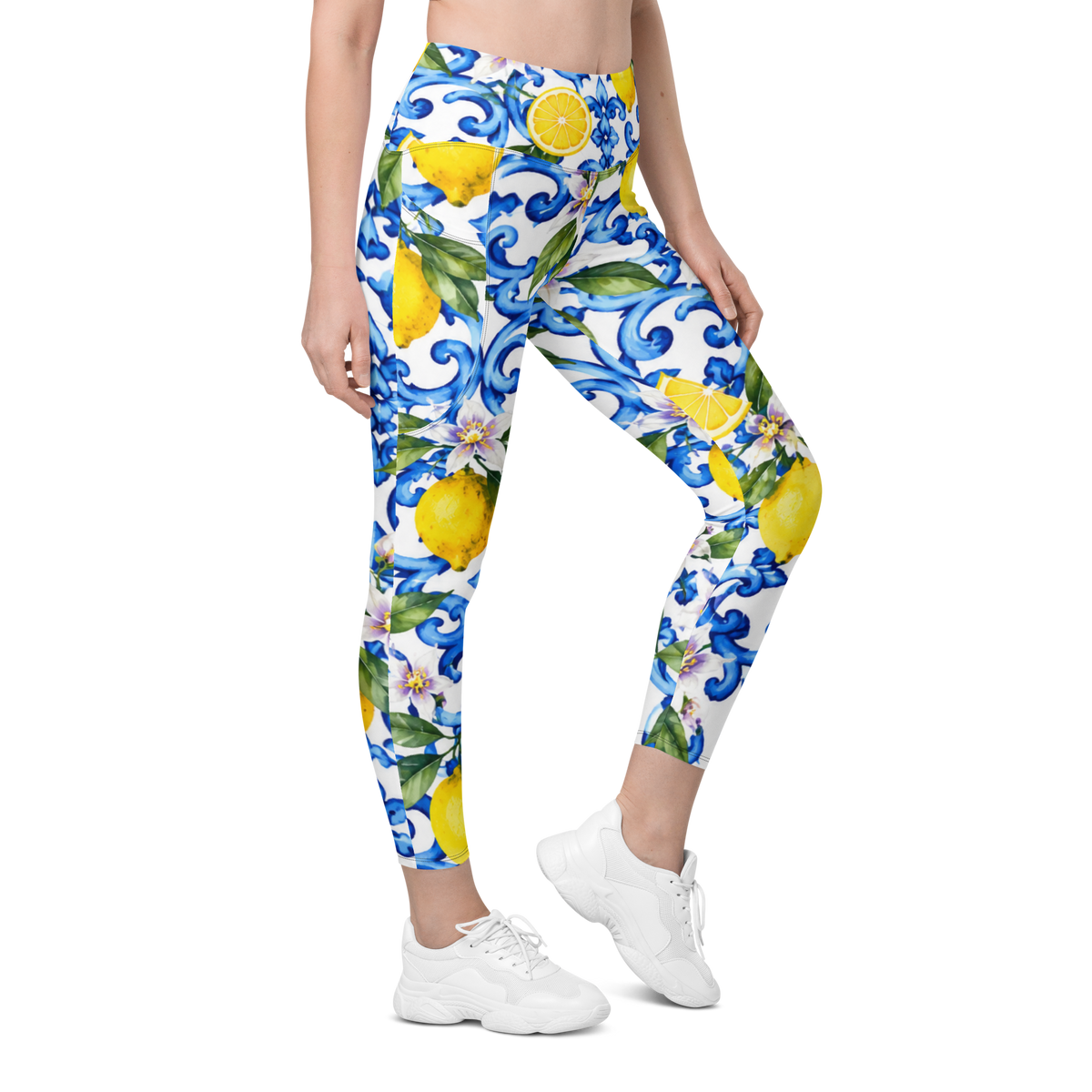 A model wearing high-waisted leggings with a vibrant blue, yellow, and green floral and lemon pattern on a white background, paired with white sneakers.