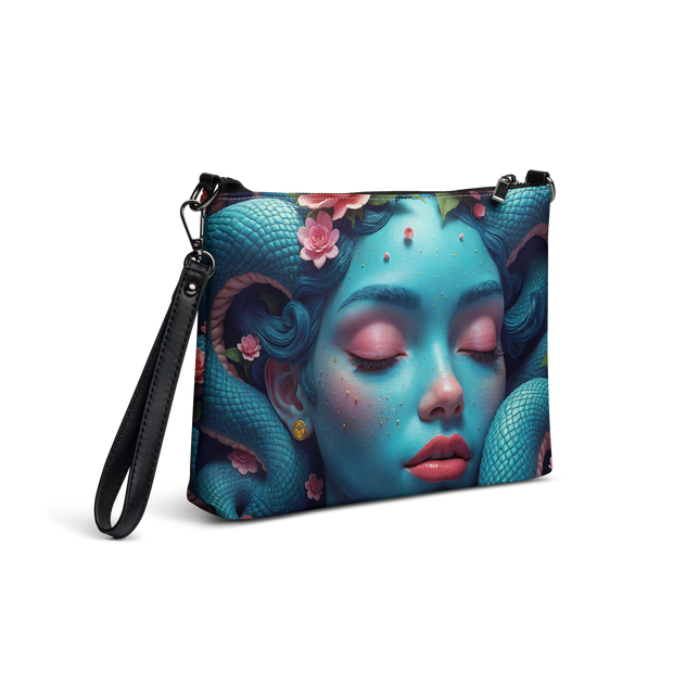 A crossbody bag featuring a vibrant, surreal graphic print of a sleeping woman's face with blue snakes and pink flowers wrapping around her, complete with a black faux-leather wrist and shoulder strap.