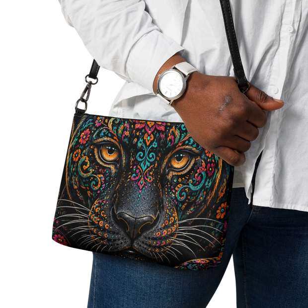 A black crossbody bag featuring a highly detailed, colorful graphic print of a leopard face with ornate mandala patterns and bright orange eyes.
