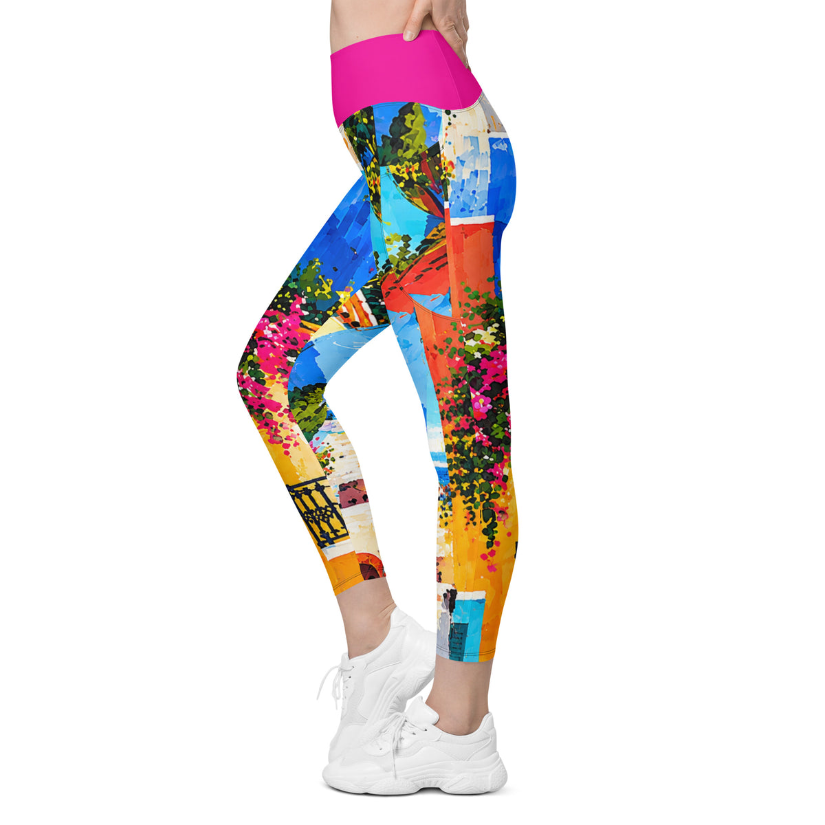 A person modeling high-waisted leggings with a vivid multicolor print of a Mediterranean-style scene, including blue sky, orange and yellow buildings, green foliage, and pink flowers, paired with white sneakers on a plain white background.