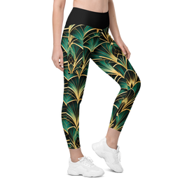 A person modeling high-waisted leggings with a bold green and gold palm leaf pattern, paired with white sneakers, on a plain white background.