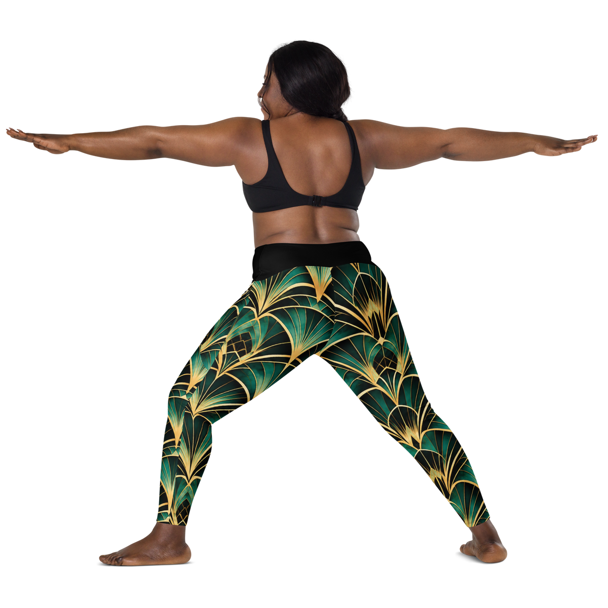 A woman poses in a yoga warrior II stance wearing high-waisted leggings with a green and gold palm leaf pattern, paired with a black sports bra, against a solid white background.