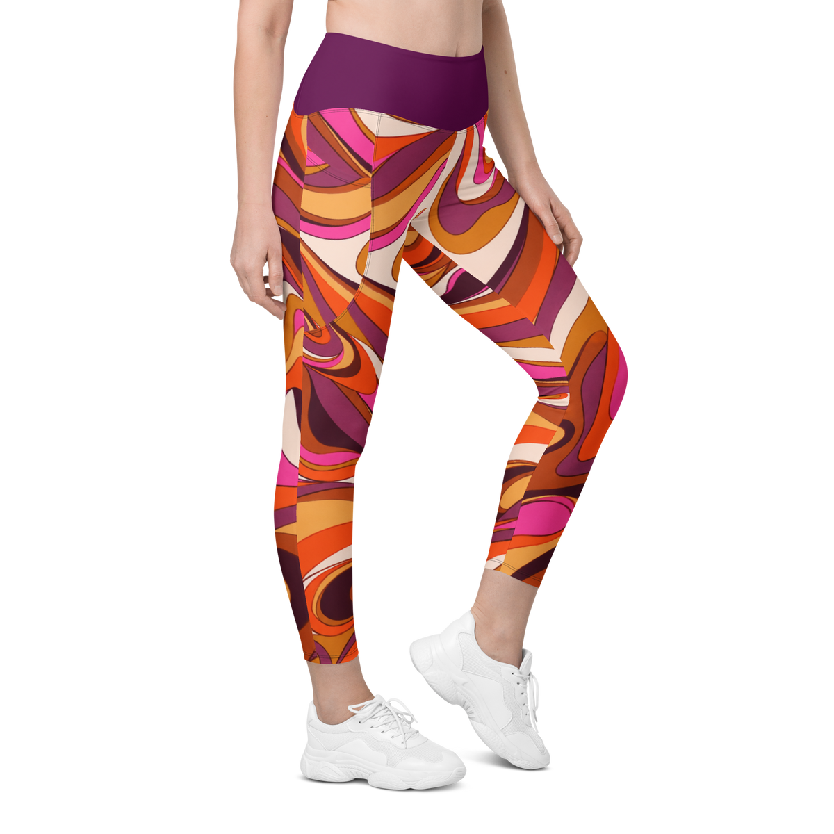 A model wearing high-waisted leggings with a bold, retro 1970s-style abstract swirl pattern in orange, pink, purple, and cream, paired with white sneakers on a solid white background.