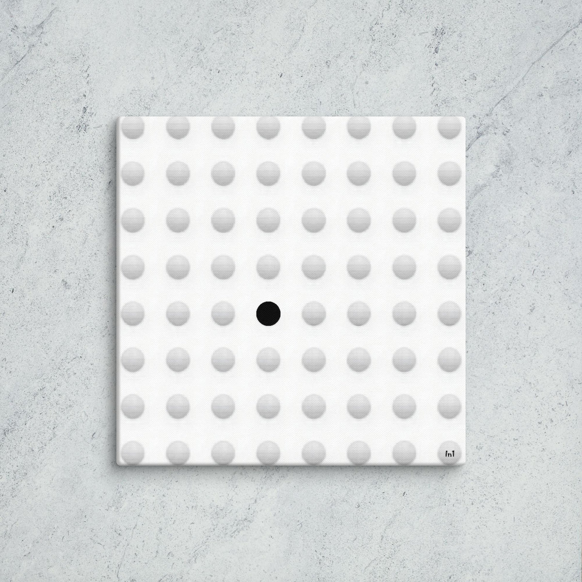 Square tile with a pattern of gray dots and one black dot on a concrete surface