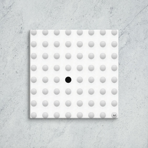 Square tile with a pattern of gray dots and one black dot on a concrete surface